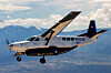 Ett enmotorigt propellerflygplan flyger över ett bergslandskap under en molnig himmel.