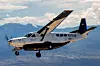 Ett enmotorigt propellerflygplan flyger över ett bergslandskap under en molnig himmel.