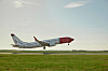 Norwegian-passagerarflygplan flyger lågt över en startbana med gräsfält i förgrunden.