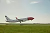 Norwegian-passagerarflygplan flyger lågt över en startbana med gräsfält i förgrunden.