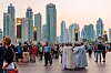 Folksamling på en promenad framför Dubais höga skyskrapor i kvällsljus.