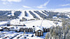 Flygbild över en snötäckt fjällanläggning med skidbackar, hotellbyggnader och skog.