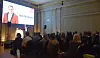 Publik lyssnar på en presentation där Nils Norberg visas på en stor skärm.