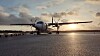 Ett turbopropflygplan står på startplattan i motljus vid solnedgång.