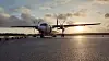 Ett turbopropflygplan står på startplattan i motljus vid solnedgång.
