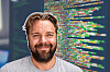 Leende skäggig man framför en datorskärm med färgrik programmeringskod.